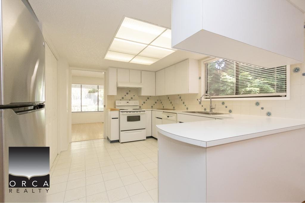 Bright kitchen with white cabinets, refrigerator, stove, and window views, ideal for Vancouver Island real estate and homebuyers.