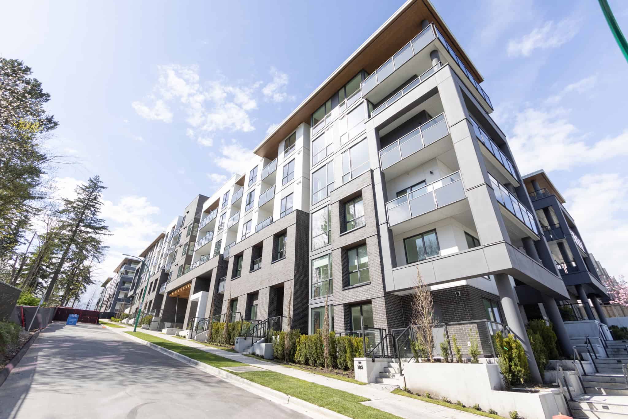 Contemporary multi-storey residential building in Vancouver with modern design, glass balconies, and lush landscaping, representing luxury real estate in BC.