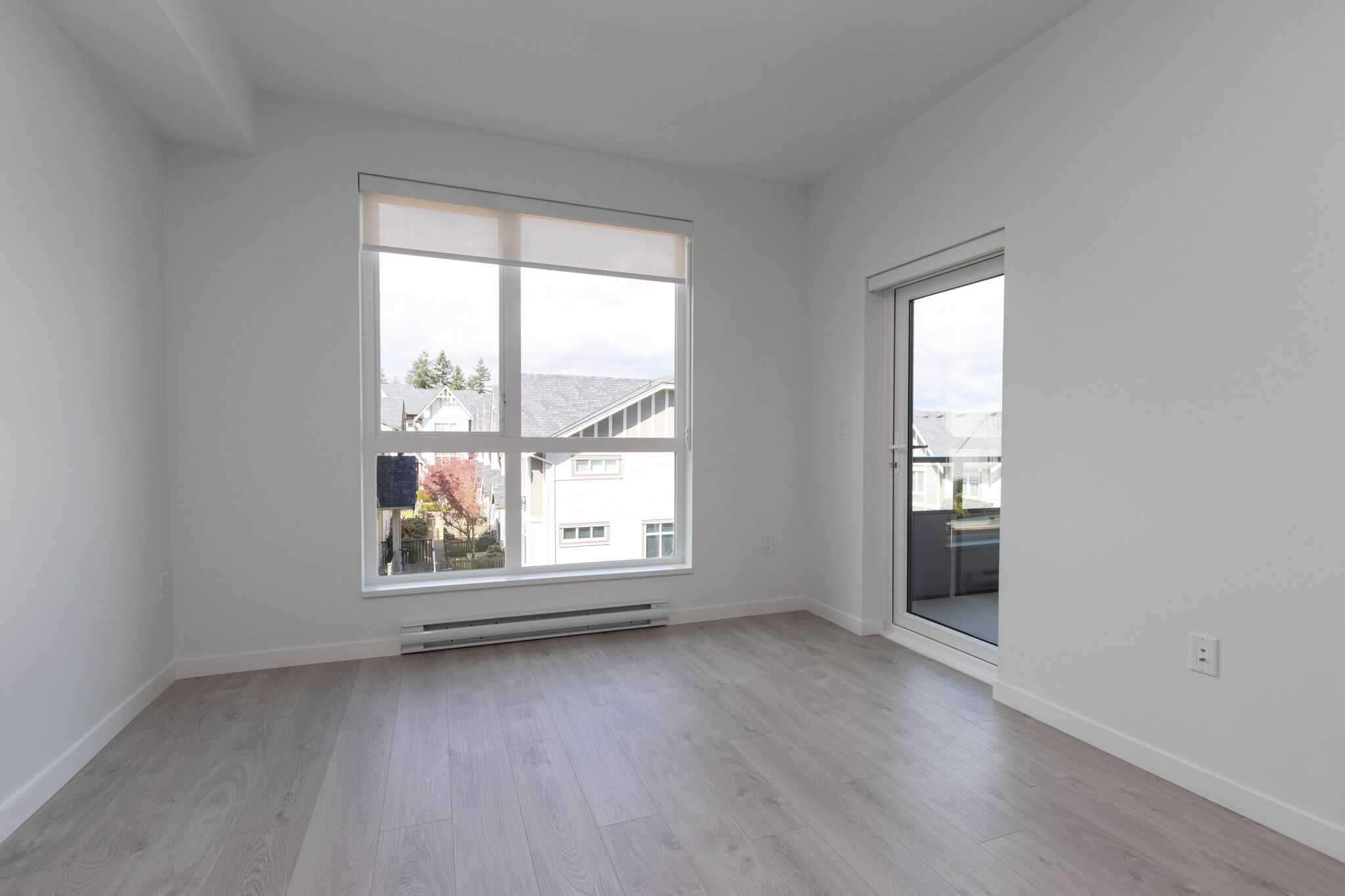 Bright, modern empty living room in a new residential property with large windows and sliding door, showcasing natural light and open space for sale by Orca Realty Inc.