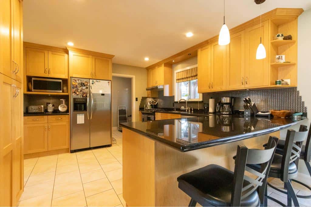 Bright kitchen with honey-colored cabinets, black granite countertops, stainless steel appliances, and cozy bar seating, ideal for homebuyers interested in modern and functional homes in BC.