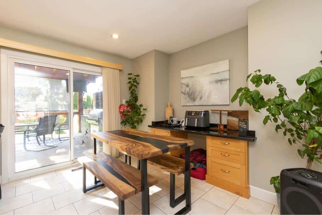 Modern dining area with sliding glass door leading to outdoor deck, featuring a wooden table, plants, and natural light, highlighting the beautiful interior of Orca Realty Inc. listings.