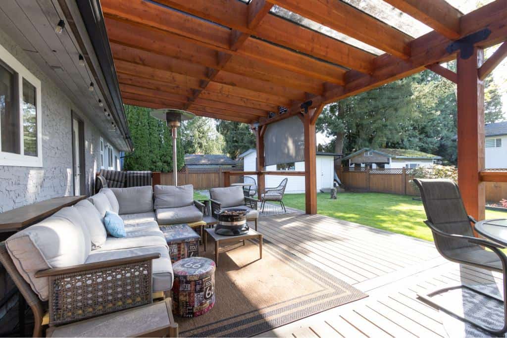Cozy outdoor deck with comfortable seating and wooden pergola, perfect for relaxing or entertaining. Backyard includes lush grass, trees, and privacy fencing, ideal for outdoor living.