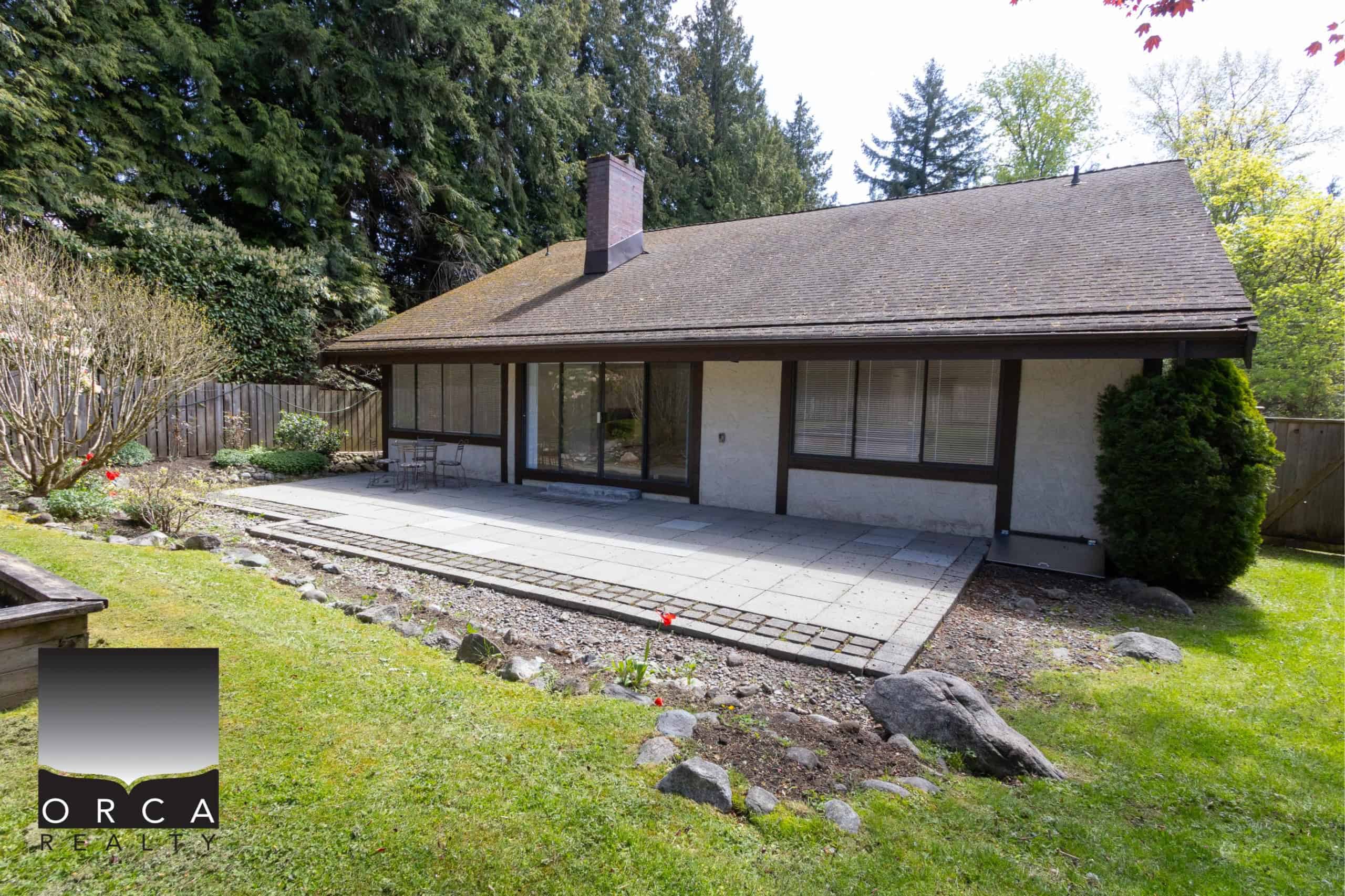 IMG_8241 Bright backyard patio with large sliding glass doors, surrounded by lush greenery and mature trees, perfect for outdoor living and entertaining in Vancouver real estate.