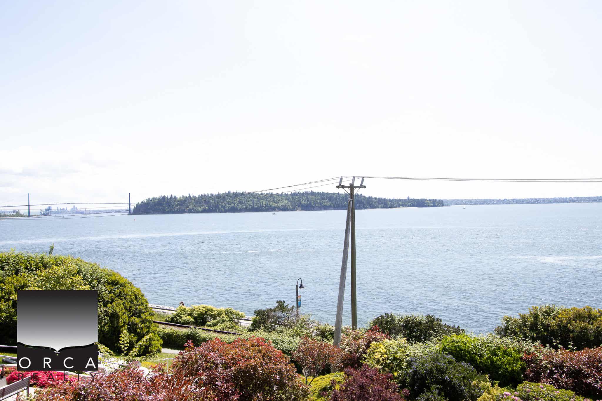 Breathtaking waterfront view from Orca Realty Inc. showcasing lush gardens, calm waters, and a clear sky, perfect for coastal living and real estate opportunities in BC.