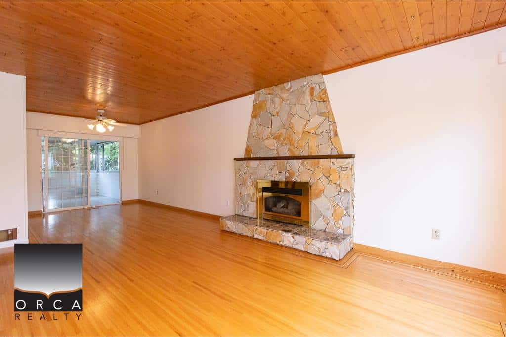 Spacious living room with wooden floors, a cozy stone fireplace, and large sliding glass doors leading to the balcony, ideal for relaxed coastal home living.