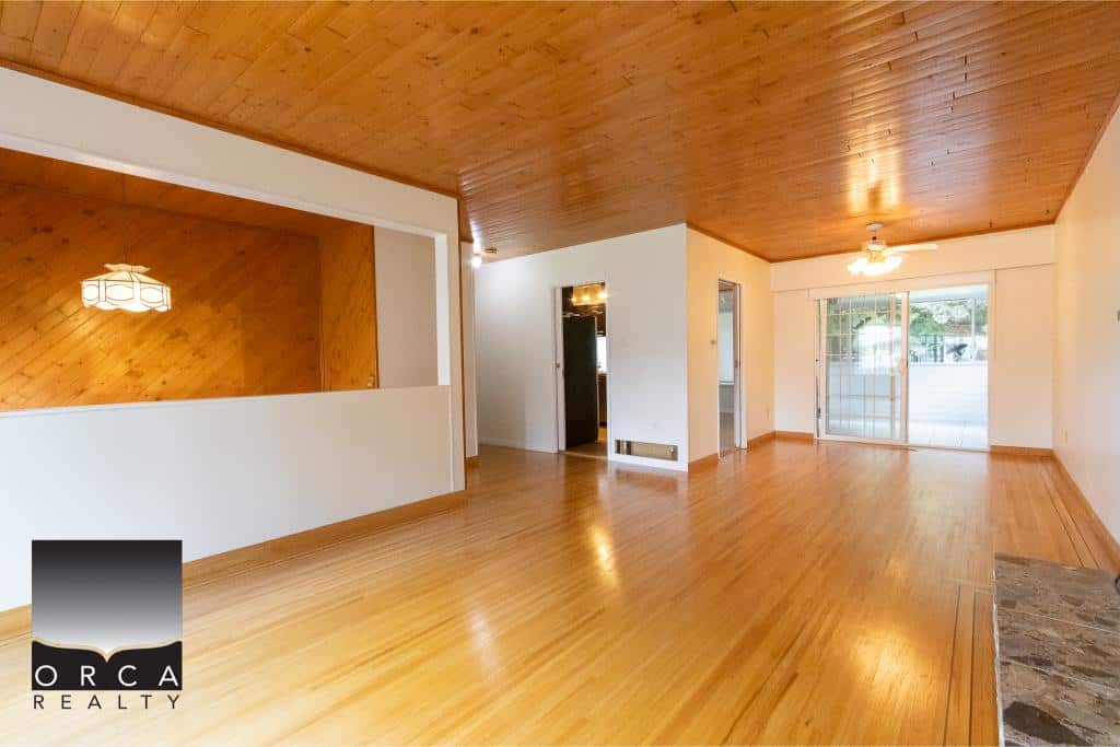 Spacious living room with wooden floors, white walls, and large sliding glass doors in a bright home listing by Orca Realty Inc.