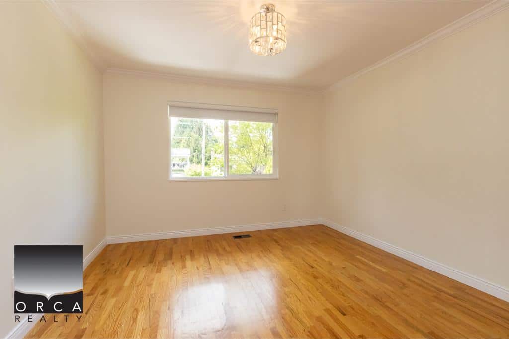 Bright empty living room with hardwood floors and large window in a residential property listed by Orca Realty Inc.