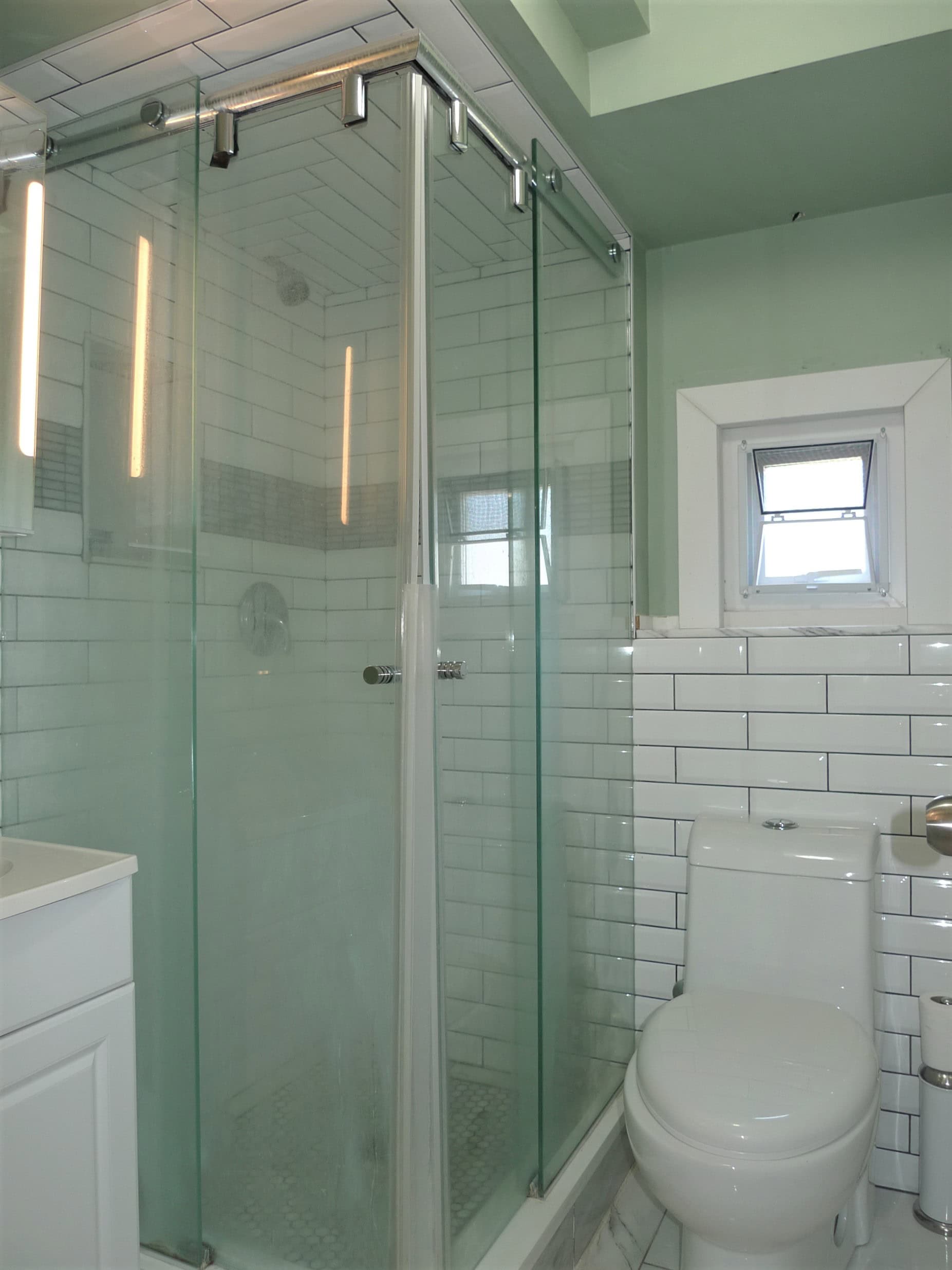 Modern bathroom with walk-in glass shower, white subway tiles, and a small window; part of Orca Realty Inc. property listings in Vancouver, BC.