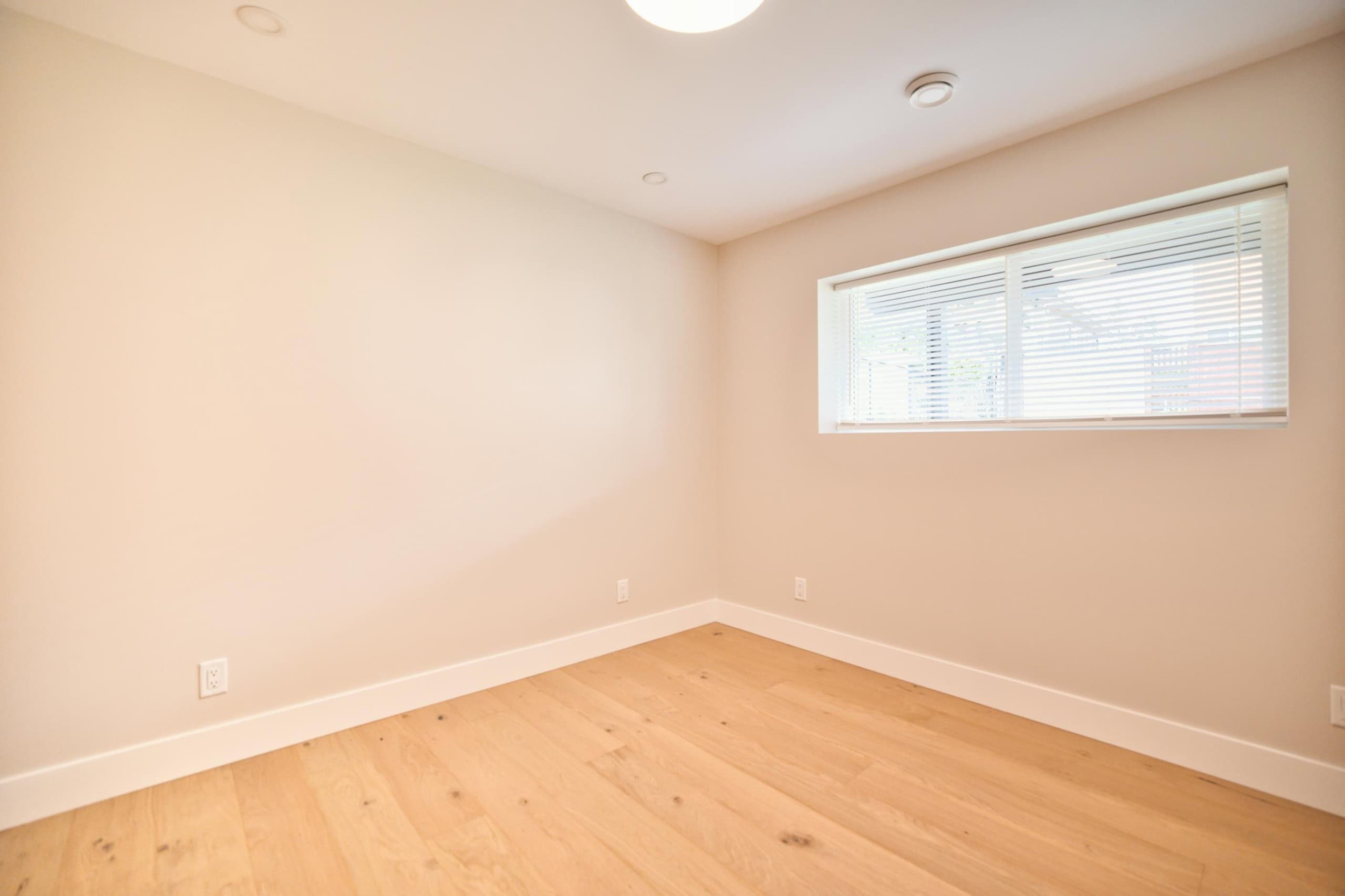Bright, spacious empty bedroom with natural light, hardwood flooring, neutral wall color, modern window blinds, perfect for Vancouver home buyers – Orca Realty Inc.