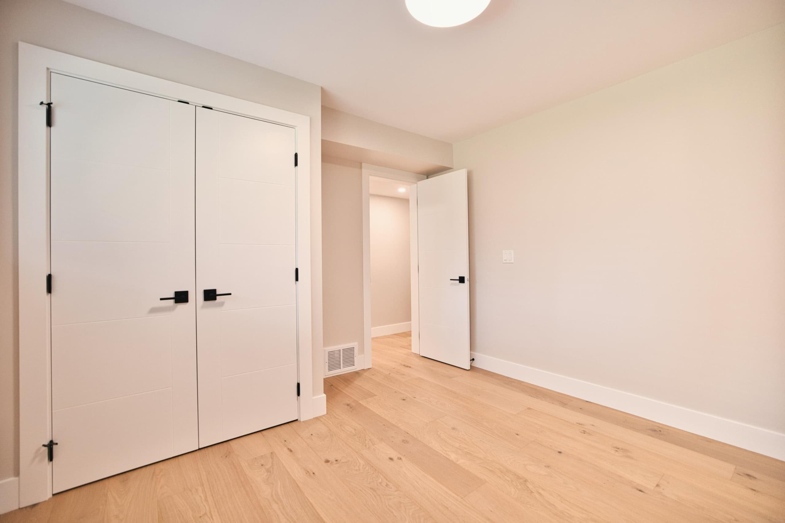 Bright modern bedroom with white double closet doors, light wood flooring, and neutral walls, ideal for Vancouver homebuyers seeking stylish and functional real estate options.