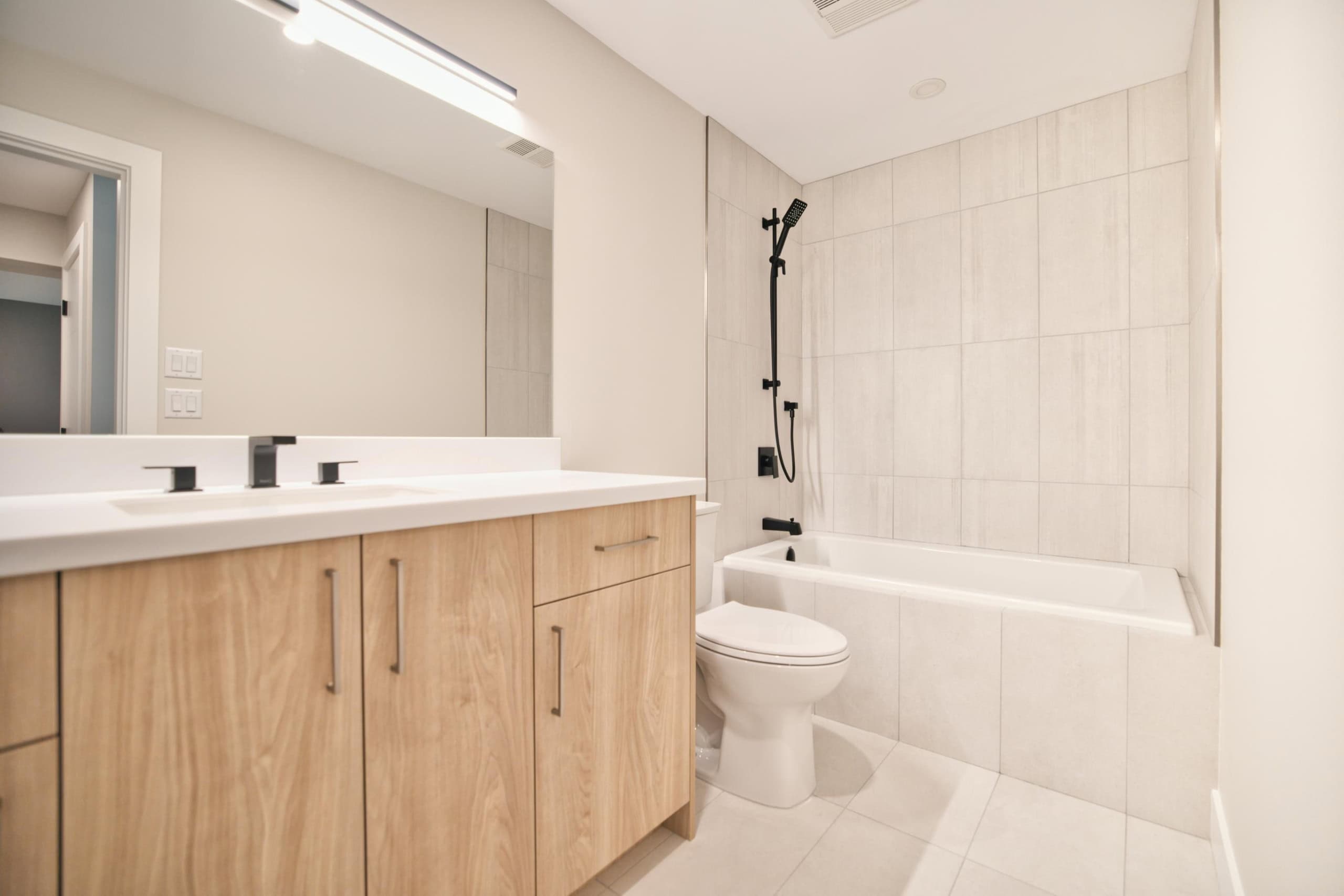 Modern bathroom with natural wood vanity, large mirror, white bathtub, and black fixtures, featuring contemporary and minimalistic design, ideal for Vancouver Island homes.