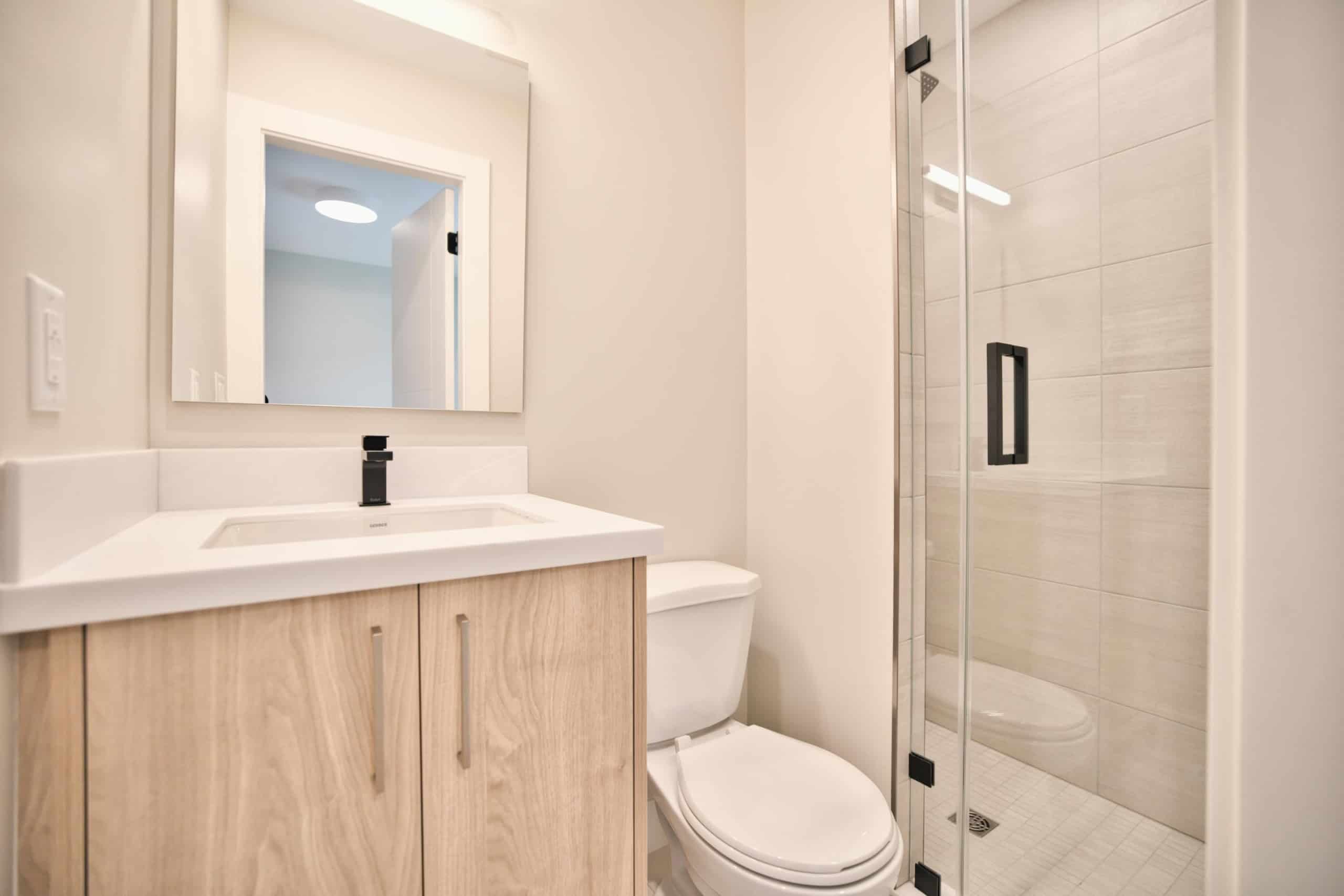 Bright modern bathroom featuring a sleek vanity with a black faucet, a white toilet, and a glass-enclosed shower with beige tiles, perfect for showcasing Vancouver Island homes for sale.