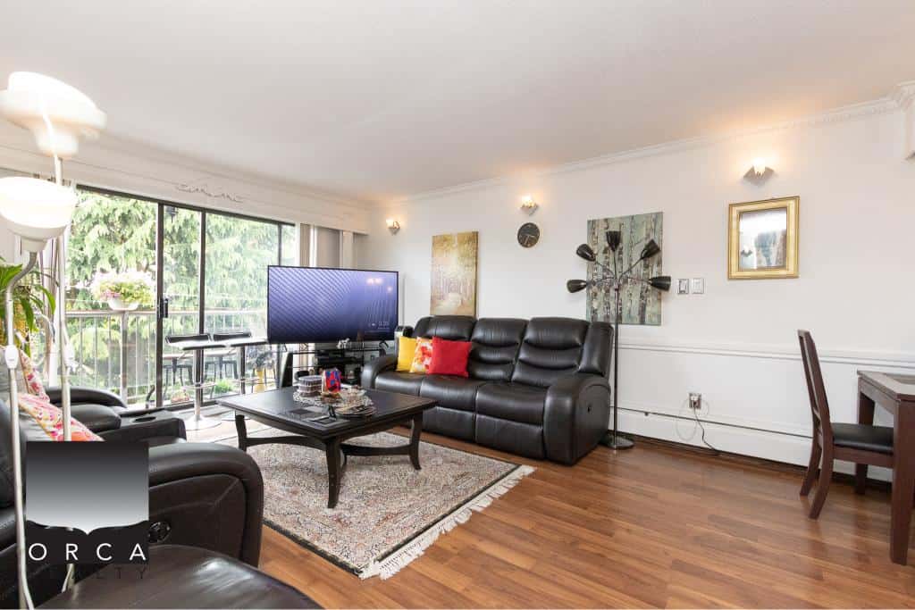 Spacious living room with large balcony, modern black leather sofas, flat-screen TV, and stylish décor, offering a comfortable setting for relaxation and entertainment in a Vancouver-area home.