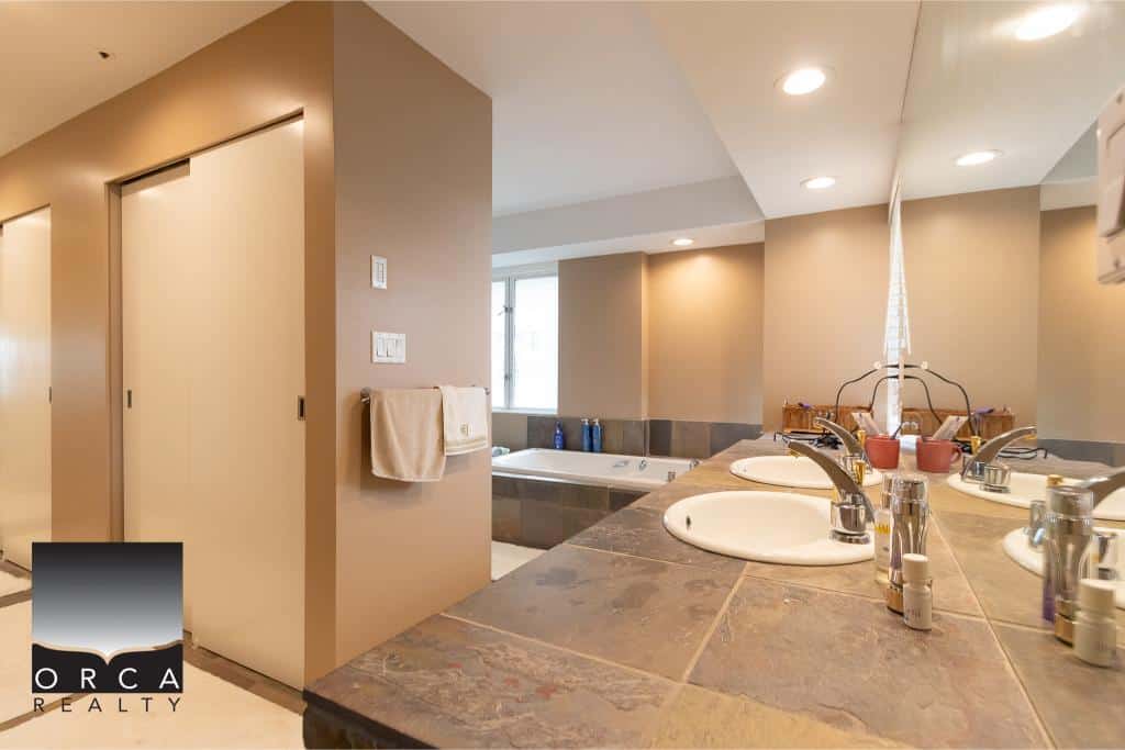 Modern bathroom with double sinks, large mirror, towels, and a relaxing bathtub in a contemporary home listing by Orca Realty Inc.
