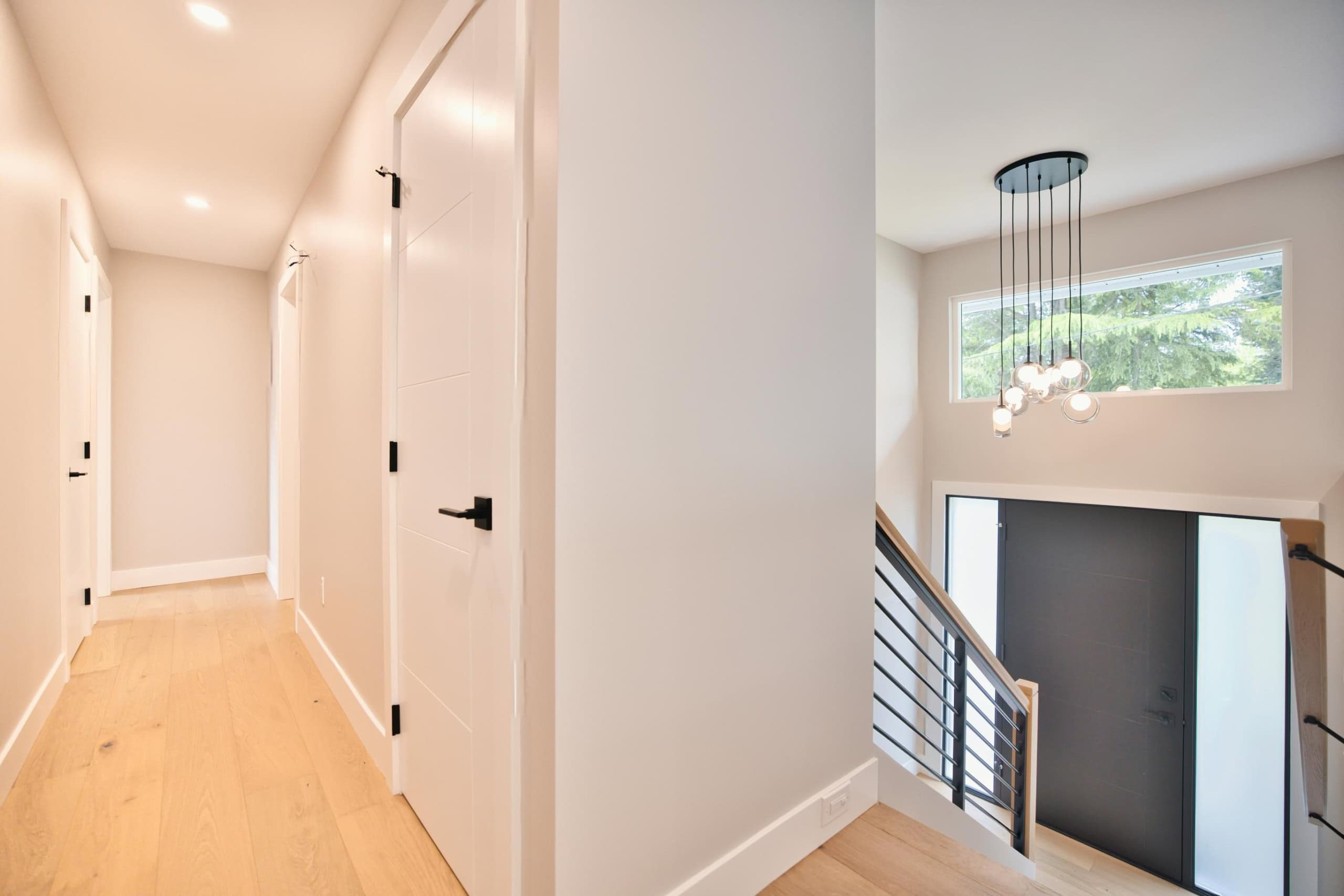 Modern interior hallway with white walls, hardwood flooring, and black door handles at Orca Realty Inc. showcasing contemporary home design.