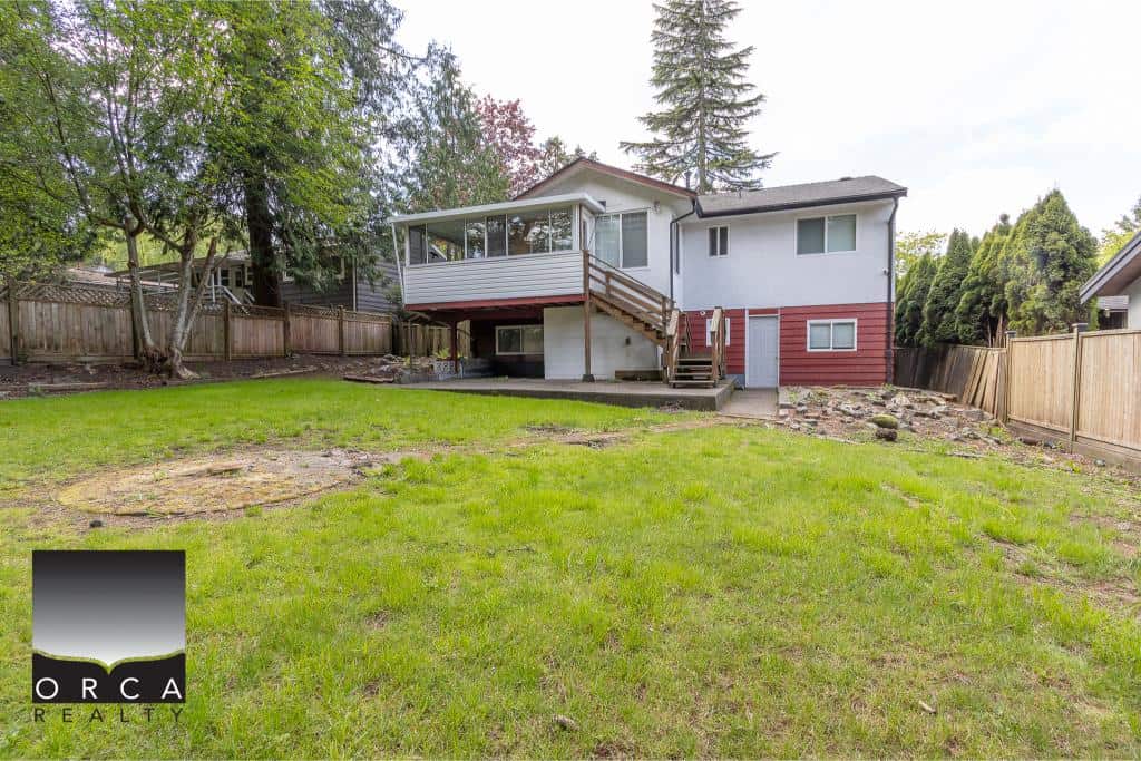 Spacious backyard of a family home with lush green grass, mature trees, and a wooden fence, ideal for outdoor activities and gardening.