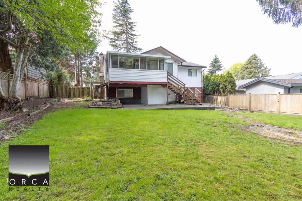 Spacious backyard view of a single-family home listed by Orca Realty Inc., showcasing lush green grass, wooden fences, and a cozy house with a raised deck, perfect for family living and outdoor activities in Vancouver.
