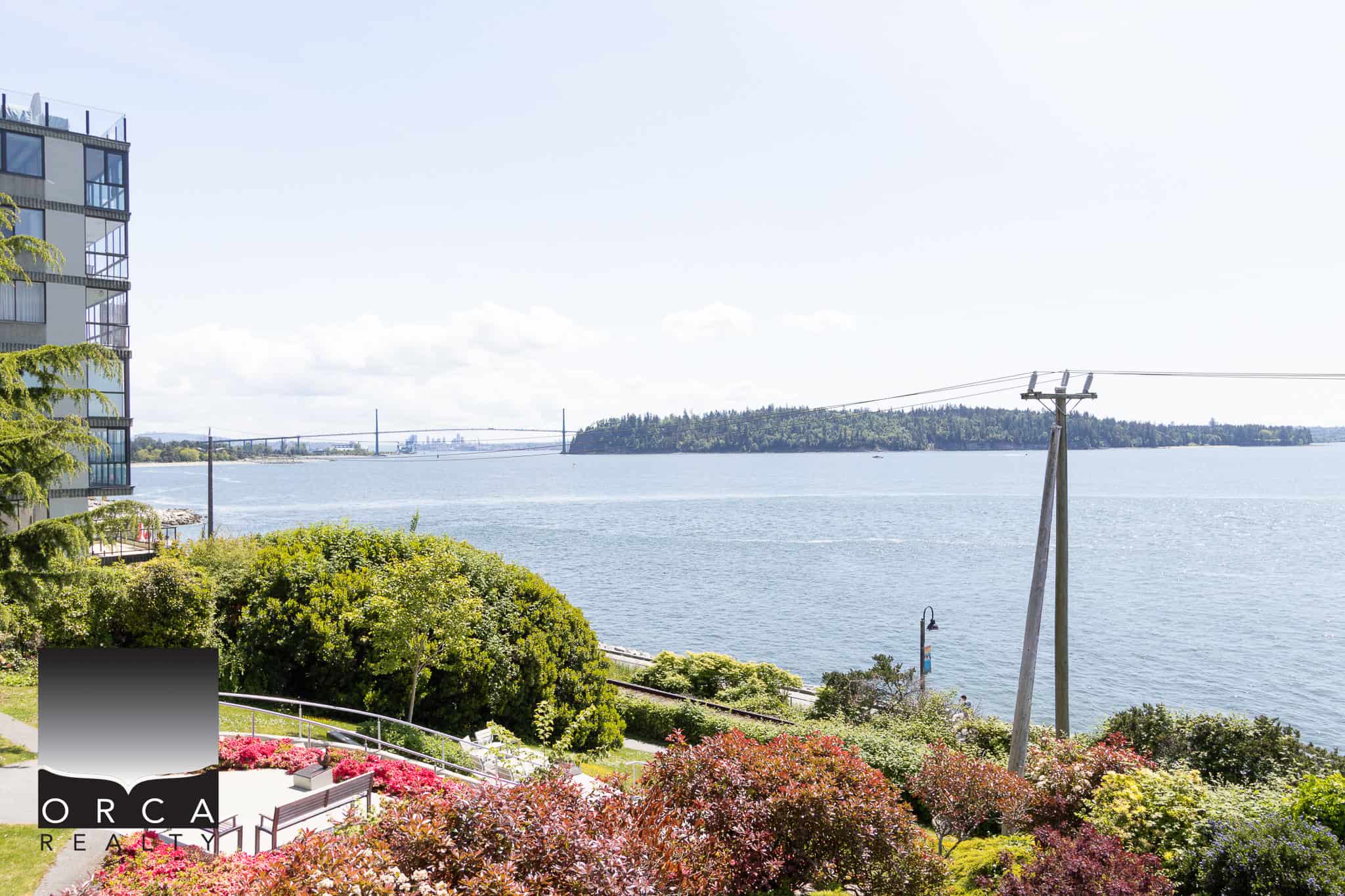 Stunning waterfront view from a modern condo in Vancouver featured by Orca Realty Inc. showcasing vibrant gardens, the Fraser River, and the iconic Lions Gate Bridge in the background.