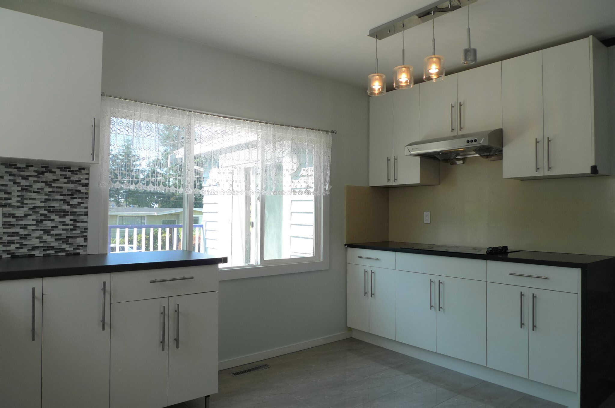 Modern kitchen with white cabinetry and black countertops, featuring a large window with lace curtains and stylish pendant lighting, perfect for Vancouver homebuyers.
