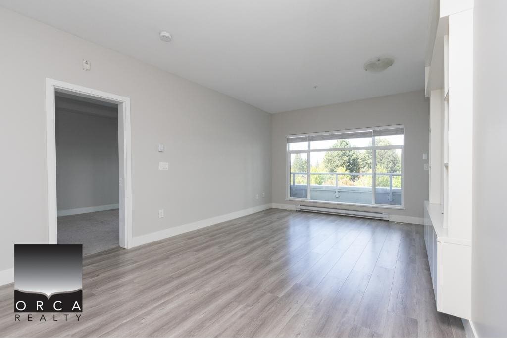 Spacious modern living room with large windows and natural light, featuring laminate flooring and neutral wall colours, ideal for homebuyers seeking contemporary Vancouver Island properties.