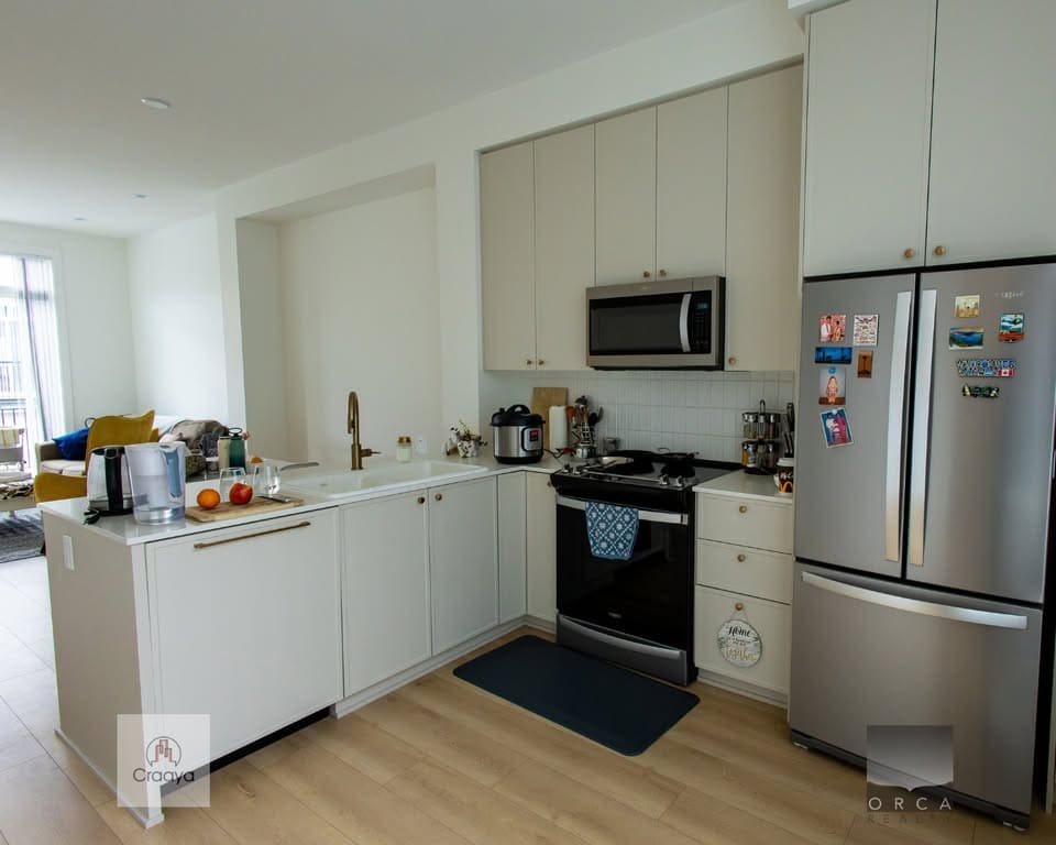 Bright modern kitchen with white cabinetry, stainless steel appliances, and a cozy open-concept living space, perfect for homebuyers in the greater Toronto area.