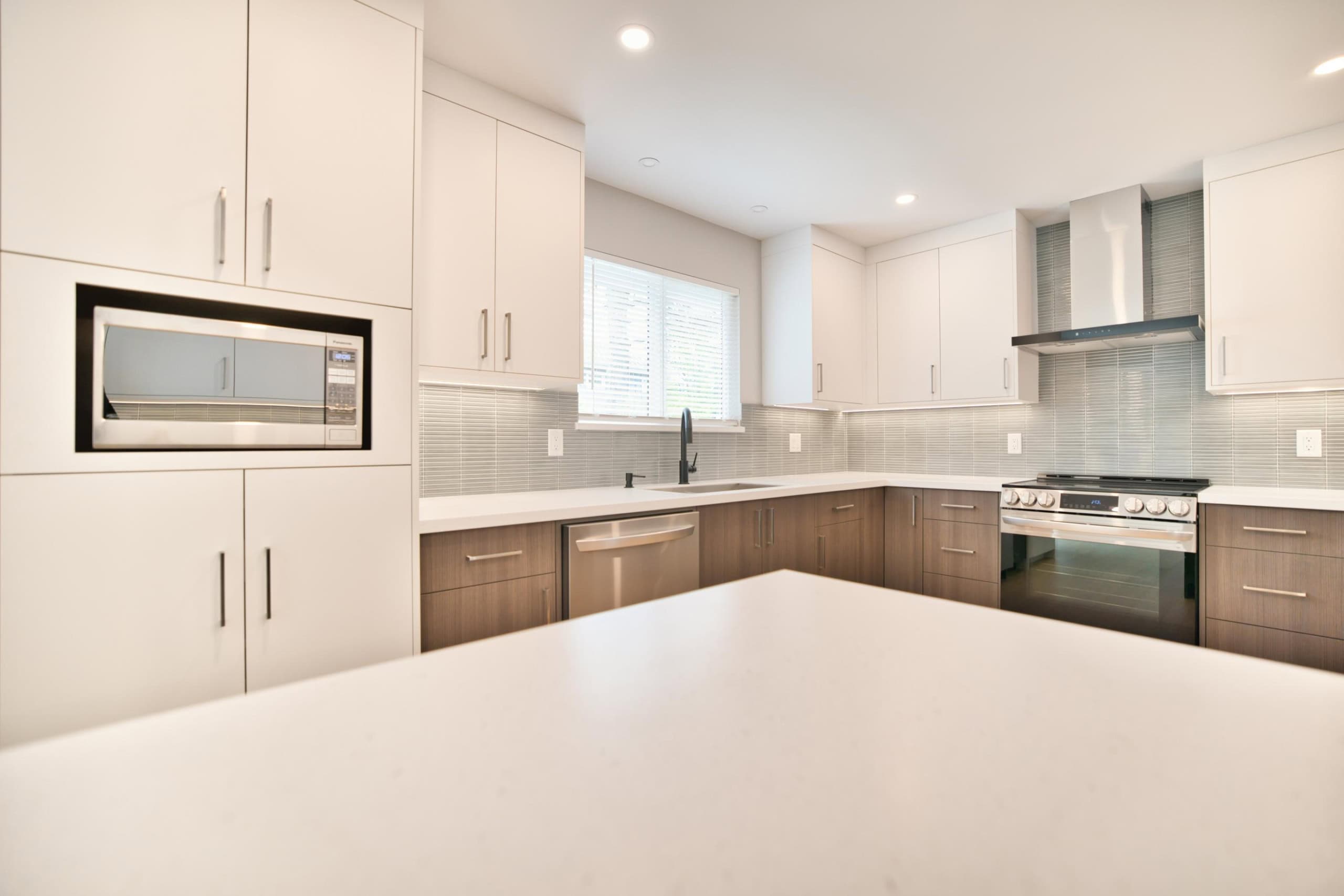 Modern kitchen with white cabinets, stainless steel appliances, and grey tile backsplash, perfect for homebuyers seeking contemporary and functional spaces.