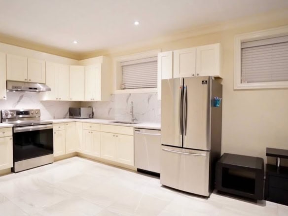 Modern white kitchen with stainless steel appliances, including a refrigerator and oven, featuring sleek cabinetry and marble backsplash, ideal for Vancouver real estate investments or family homes.