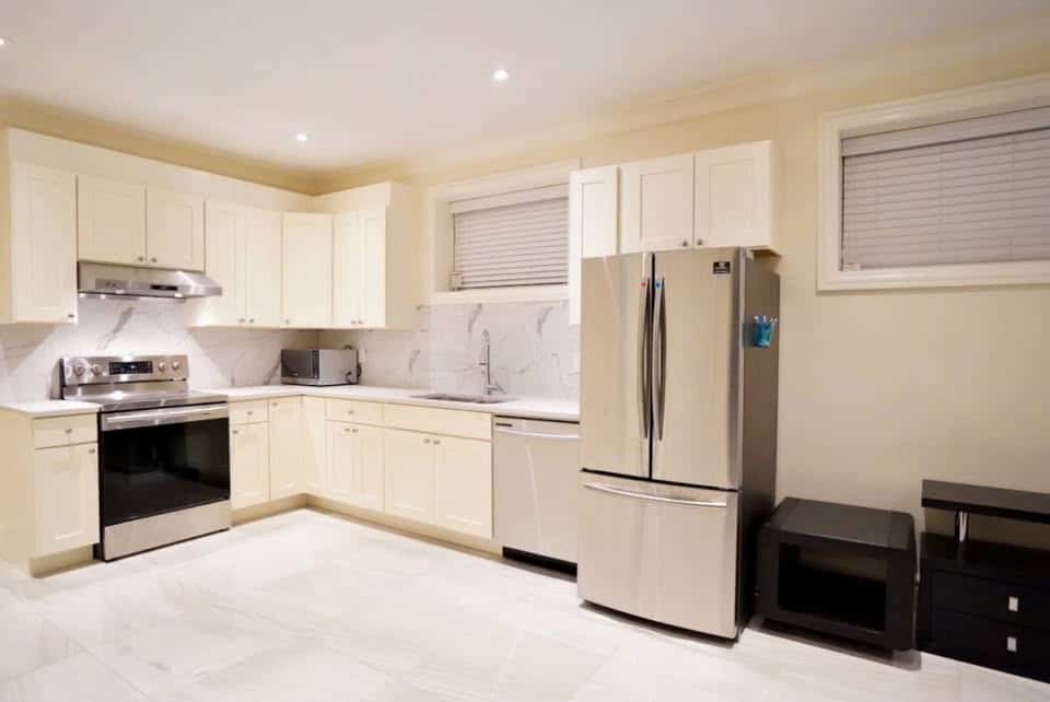Modern white kitchen with stainless steel appliances, including a refrigerator and oven, featuring sleek cabinetry and marble backsplash, ideal for Vancouver real estate investments or family homes.