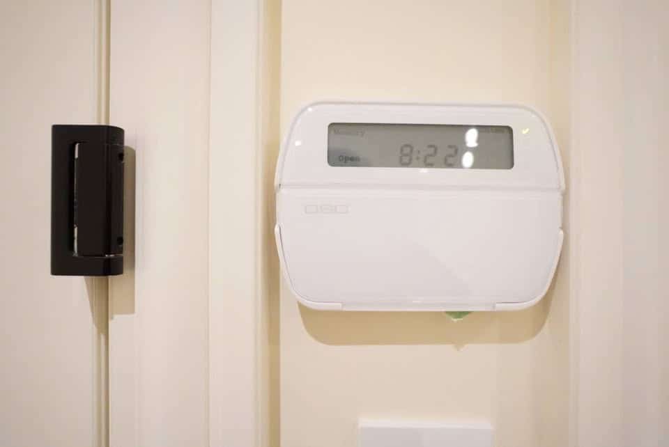 Smart home security system digital alarm control panel mounted on a beige wall.