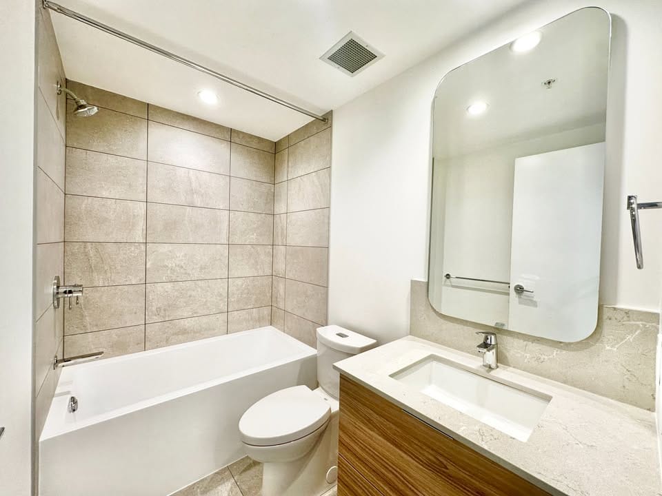 Modern bathroom with tiled shower and bathtub, white toilet, and contemporary vanity with marble countertop and large mirror, showcasing stylish and functional interior design in a Vancouver property.