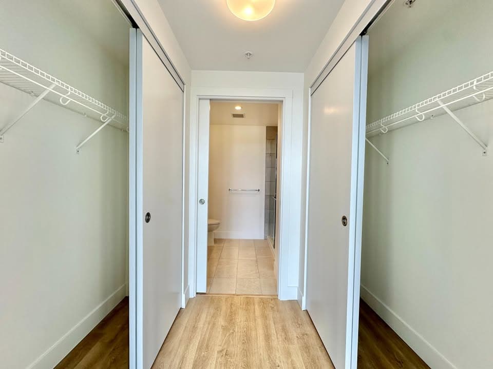 Spacious walk-in closet with white wire shelving in a modern home or condo. Bright, clean interior with sliding closet doors and hardwood flooring. Perfect for storage and organization.