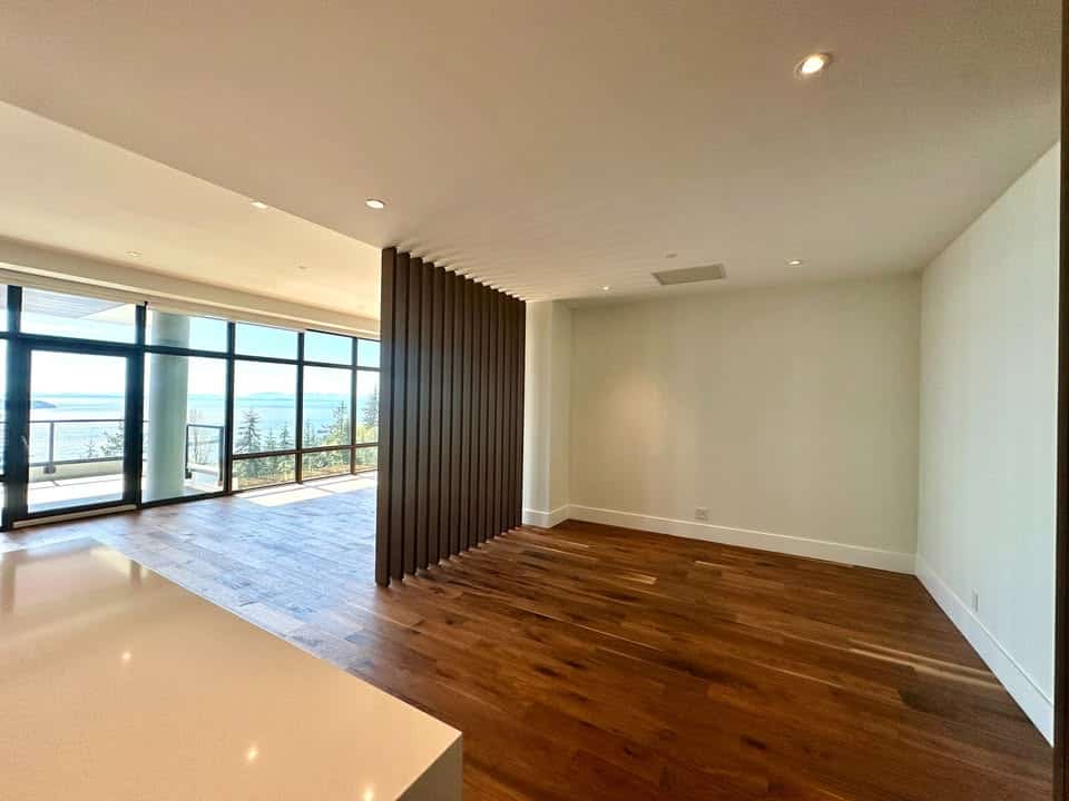 Bright modern living space with expansive ocean views and sleek interior design featuring hardwood floors and a stylish wooden room divider. Perfect for upscale Vancouver-area homes.