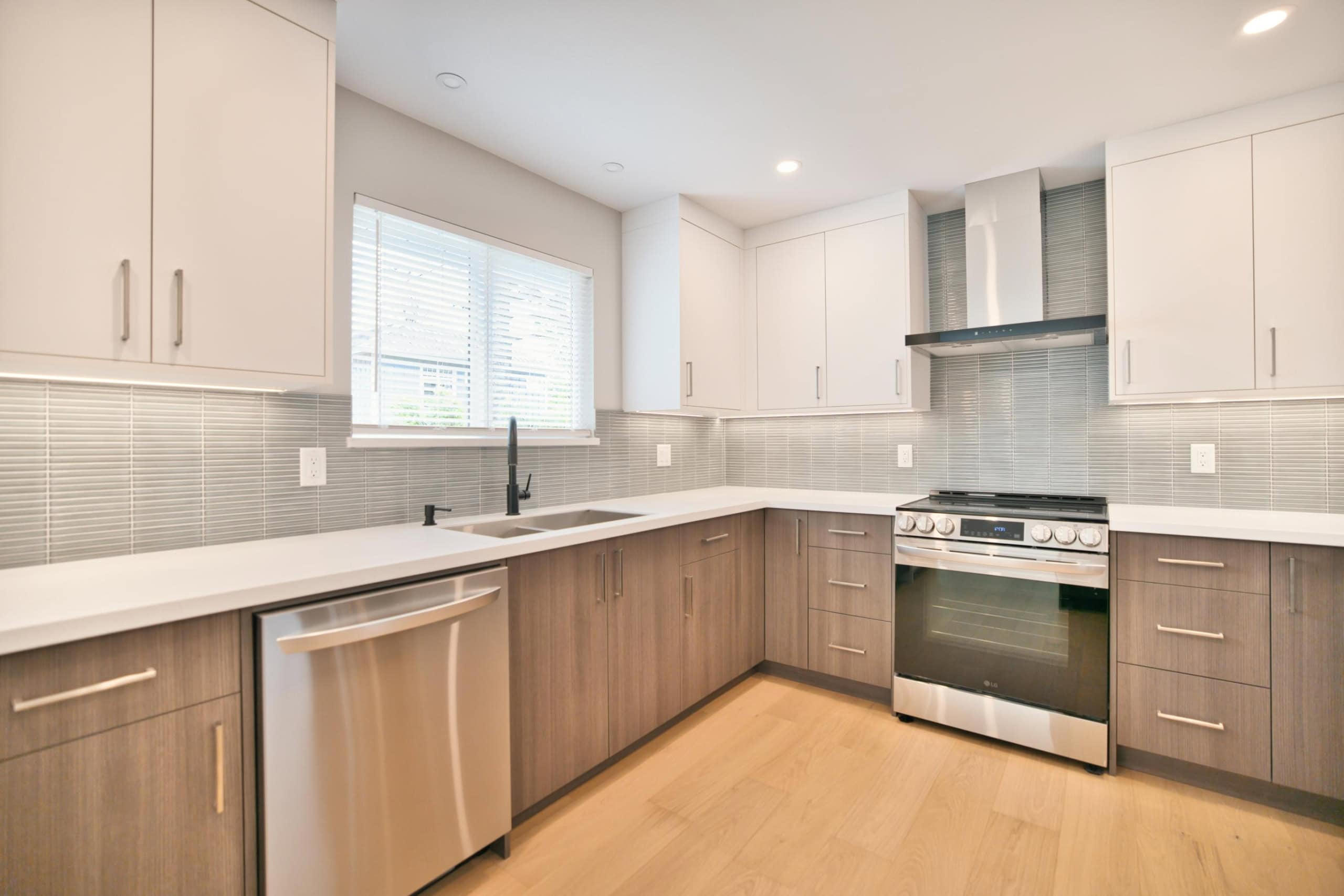 Modern kitchen with white upper cabinets, wood lower cabinets, stainless steel appliances, and a neutral tile backsplash, perfect for Vancouver homebuyers.