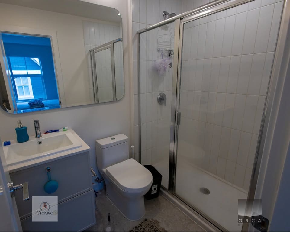 Bright modern small bathroom with white tiles, glass shower enclosure, vanity with sink, and toilet – ideal for Vancouver real estate properties.
