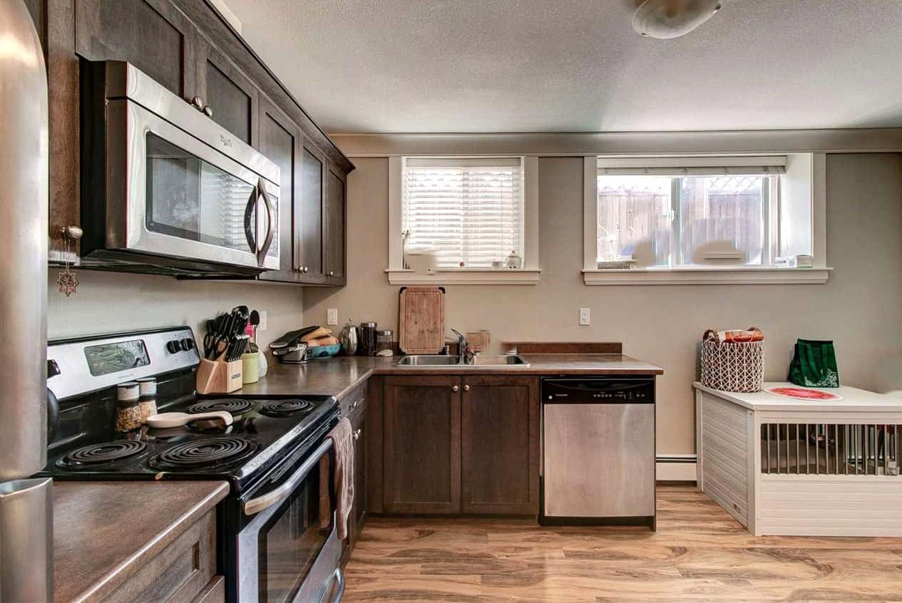 Modern kitchen with dark wood cabinets, stainless steel microwave, electric stove, and natural light from two windows, featuring hardwood floors and functional space.