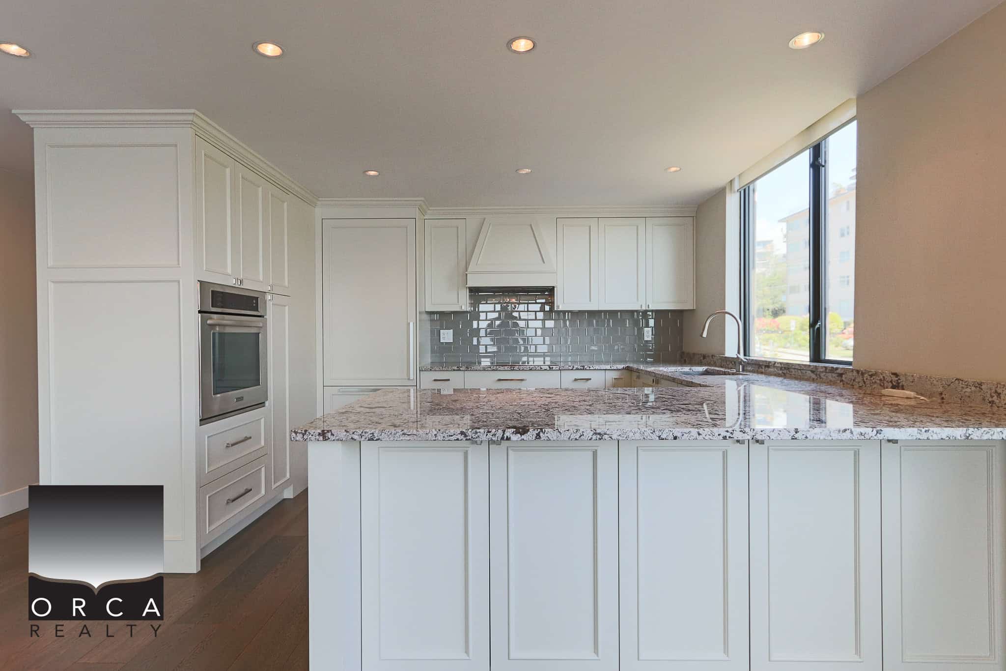 Modern kitchen with granite countertops, white cabinetry, stainless steel appliances, and a large window for natural light, perfect for Vancouver Island real estate listings.
