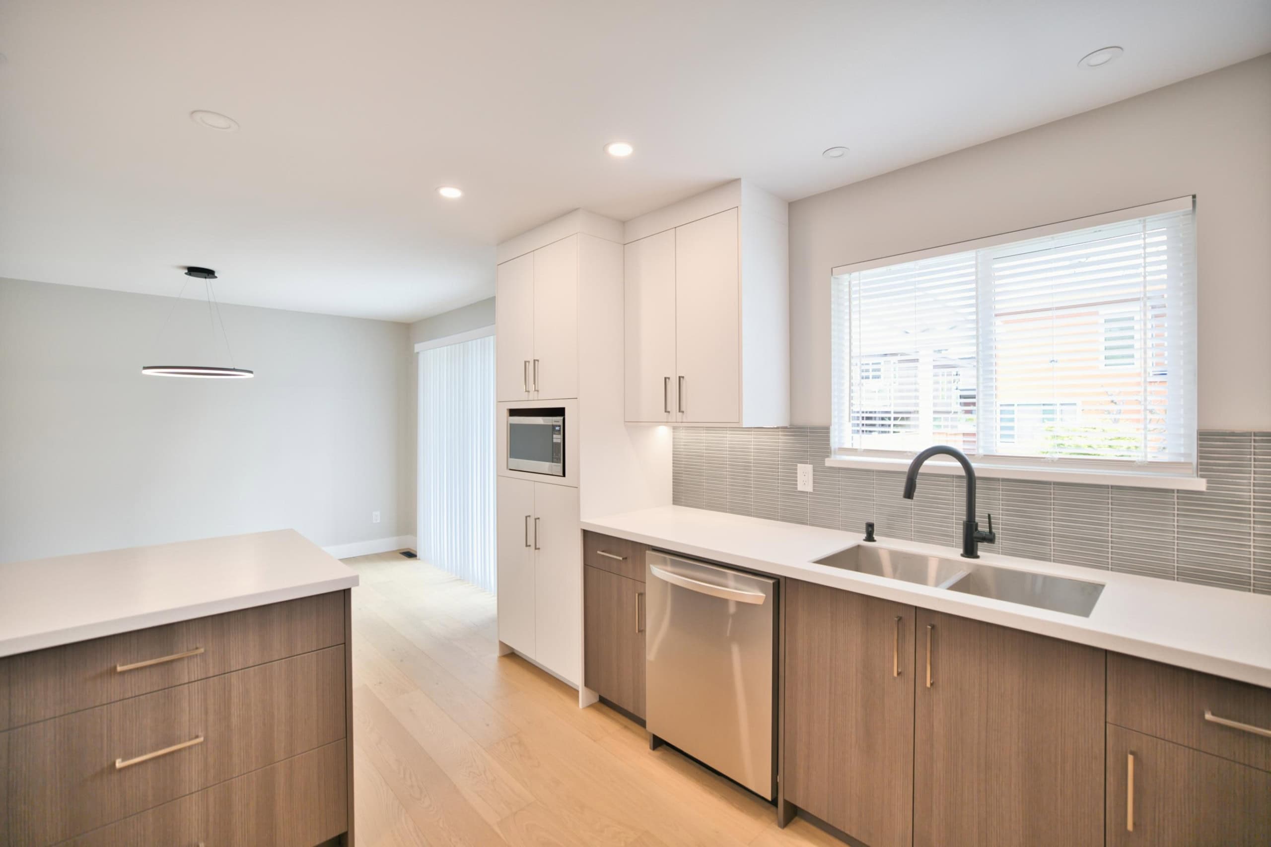 Bright modern kitchen with white cabinets, stainless steel appliances, and large window, showcasing contemporary home design by Orca Realty Inc.