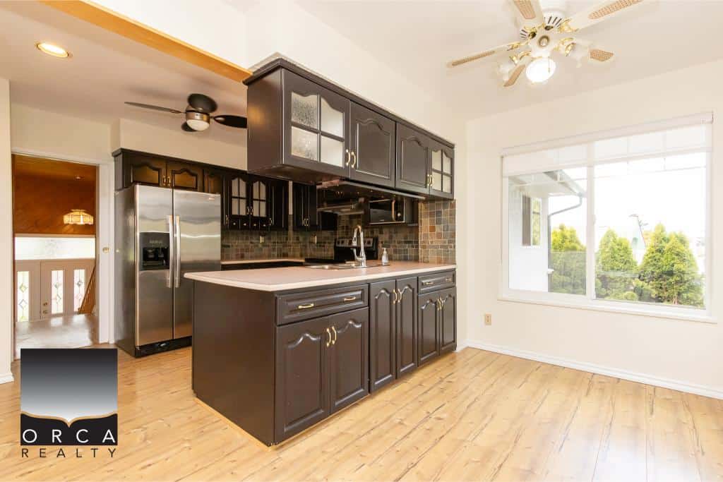 Spacious kitchen with black cabinetry, stainless steel fridge, and large window overlooking backyard - ideal for homebuyers seeking modern kitchens.