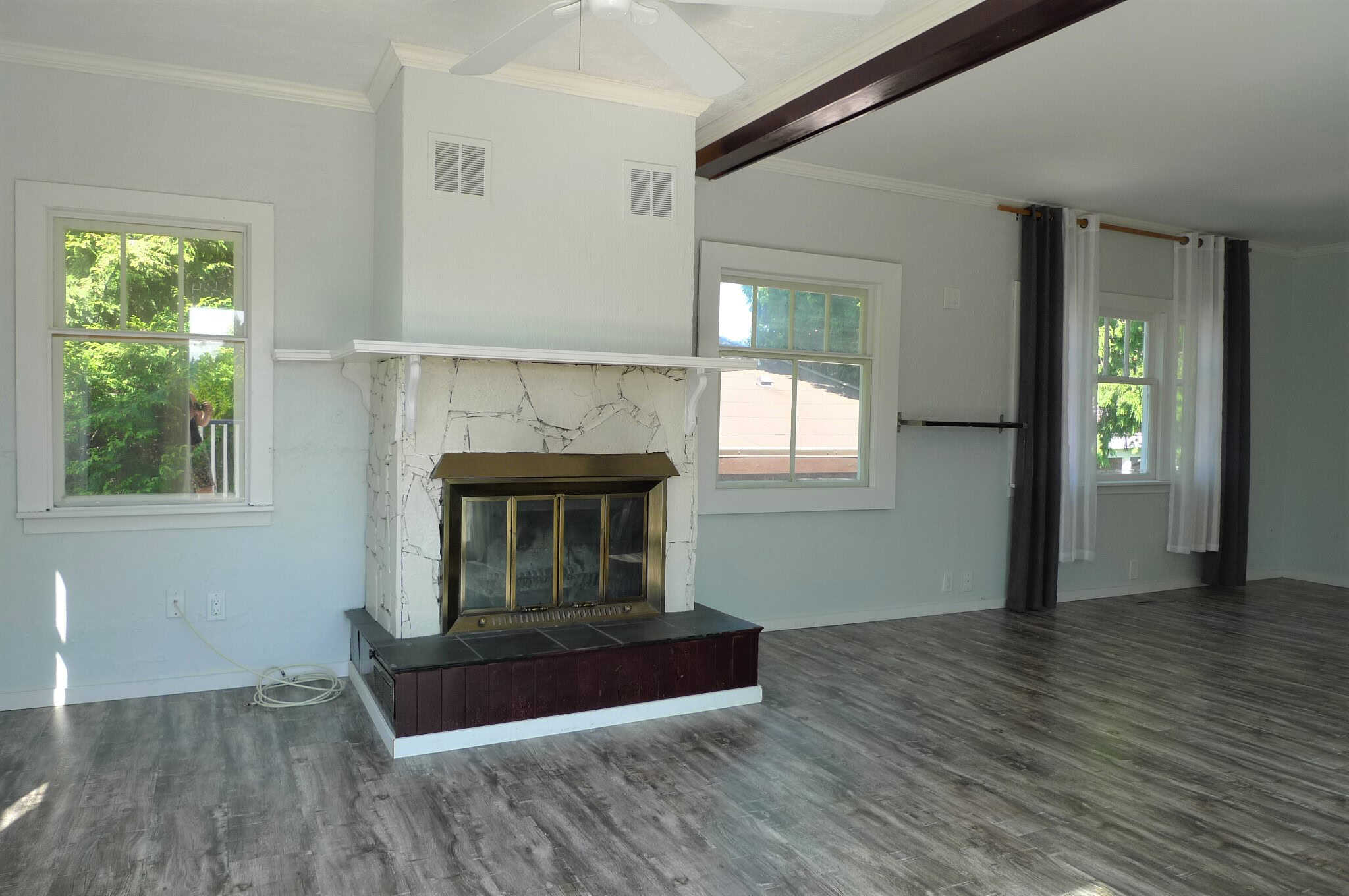 Bright living room with white walls, large windows, and a cozy fireplace featuring a marble surround and brass accents, showcasing a spacious and inviting atmosphere.