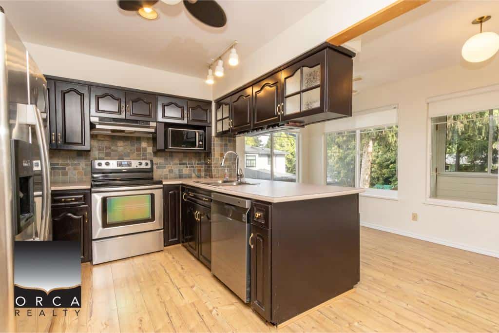 Modern kitchen with black cabinetry, stainless steel appliances, and natural light, ideal for Vancouver Island real estate listings.