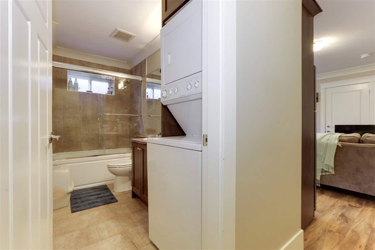 Stacked washer and dryer unit in a compact laundry area, adjacent to a bathroom with a glass shower enclosure, modern fixtures, and hardwood flooring, located within a cozy, well-maintained home.