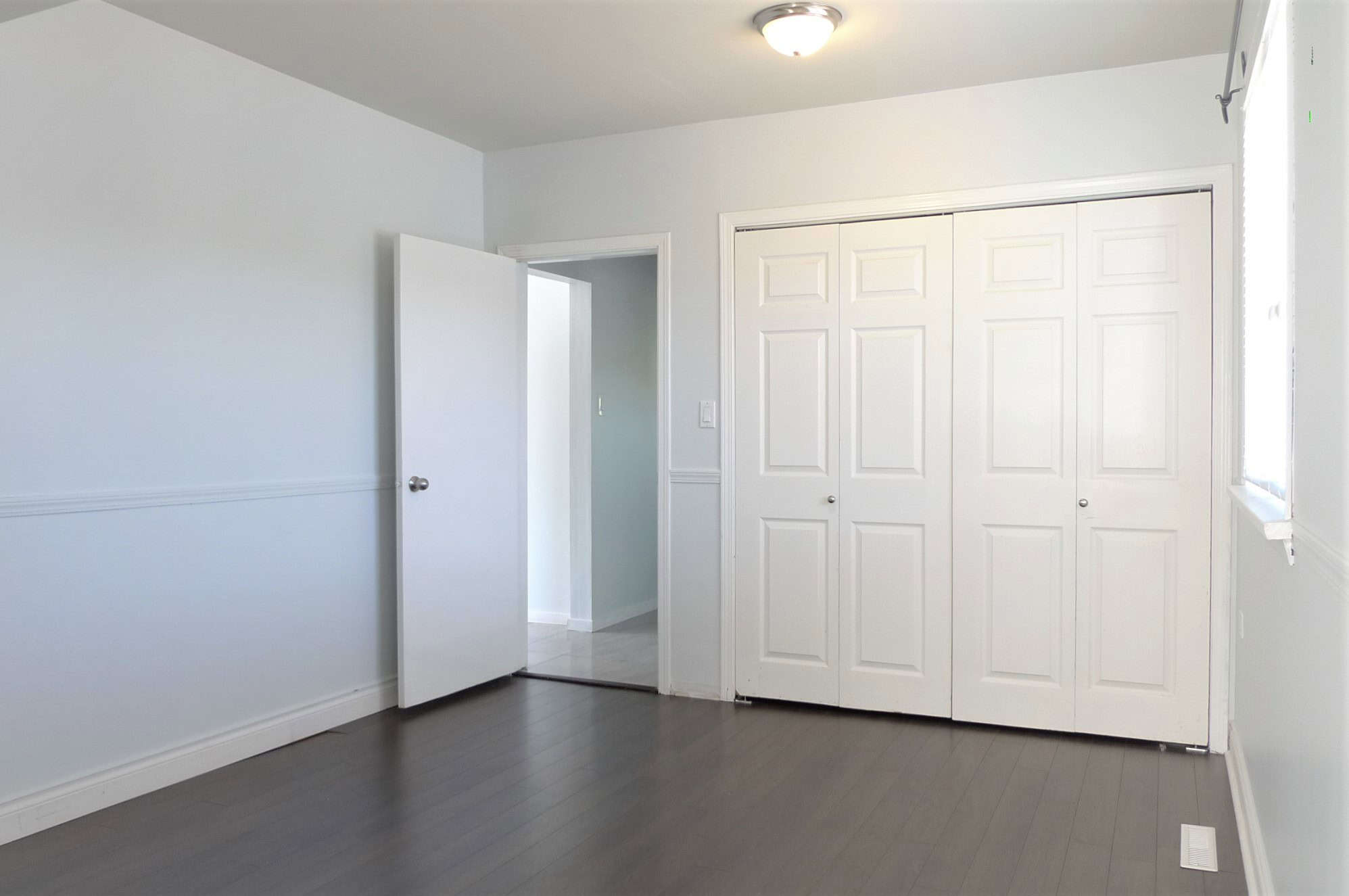 Bright empty bedroom with white walls, hardwood flooring, built-in closet, and natural light in an Orca Realty Inc. property.