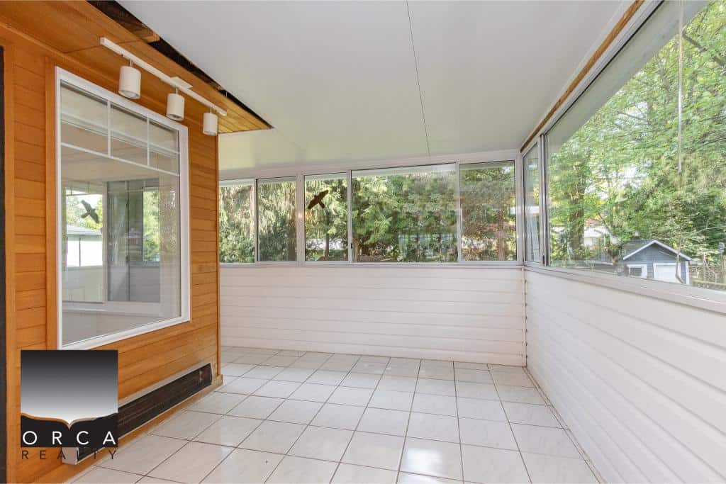 Bright enclosed porch with large windows overlooking trees, perfect for relaxing or outdoor entertaining, attached to a home listed by Orca Realty Inc. in Vancouver.