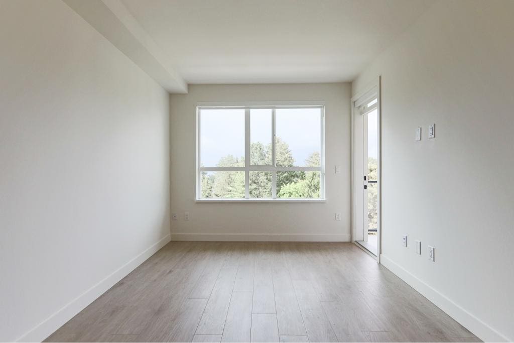 Bright, modern empty living room with large window and balcony door, featuring neutral decor, light wood flooring, ideal for Vancouver real estate listings.