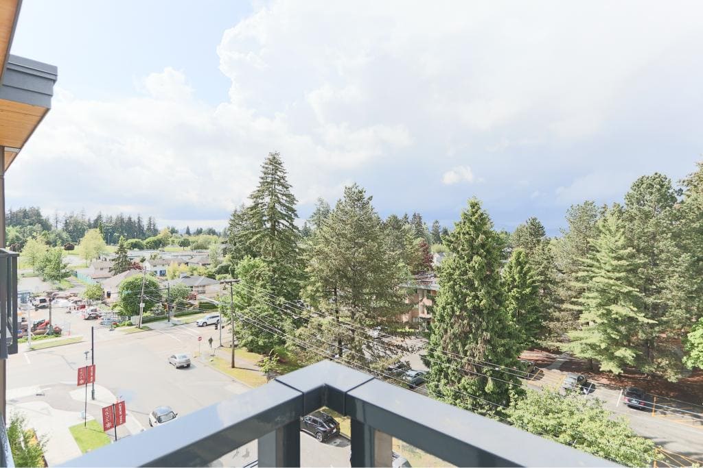 Vancouver city view from a balcony, showcasing lush trees, residential buildings, and a quiet street, ideal for real estate buyers and investors interested in the Vancouver market.