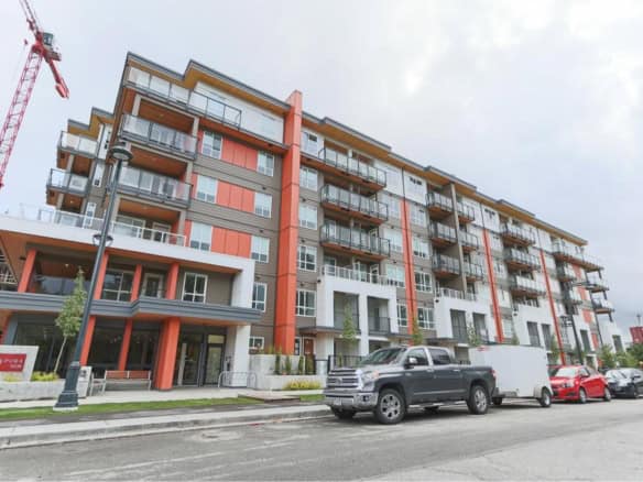 Modern multi-story condo building with commercial spaces at street level, located in a vibrant urban area, featuring balconies and contemporary architecture.