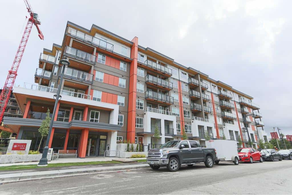 Modern multi-story condo building with commercial spaces at street level, located in a vibrant urban area, featuring balconies and contemporary architecture.