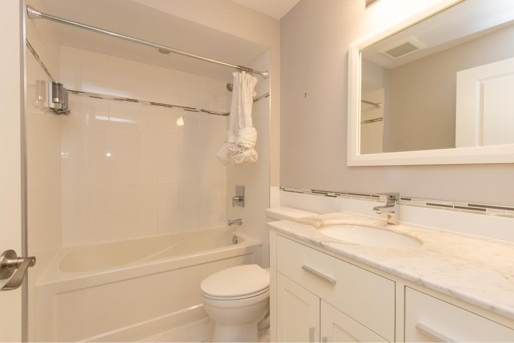 Modern bathroom with bathtub, white tile, marble vanity, large mirror, and neutral decor, ideal for Vancouver real estate listings and home staging.