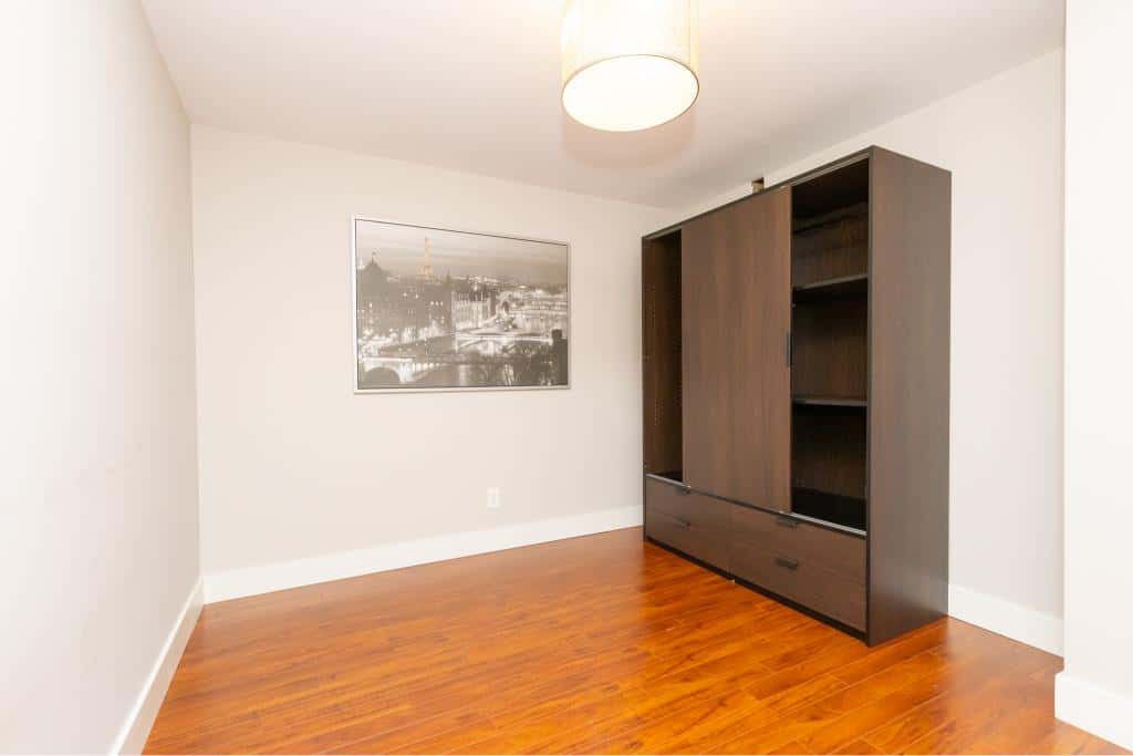 Modern empty room with hardwood flooring, featuring a dark wooden wardrobe and black-and-white cityscape print wall art, perfect for Vancouver or Victoria real estate listings.