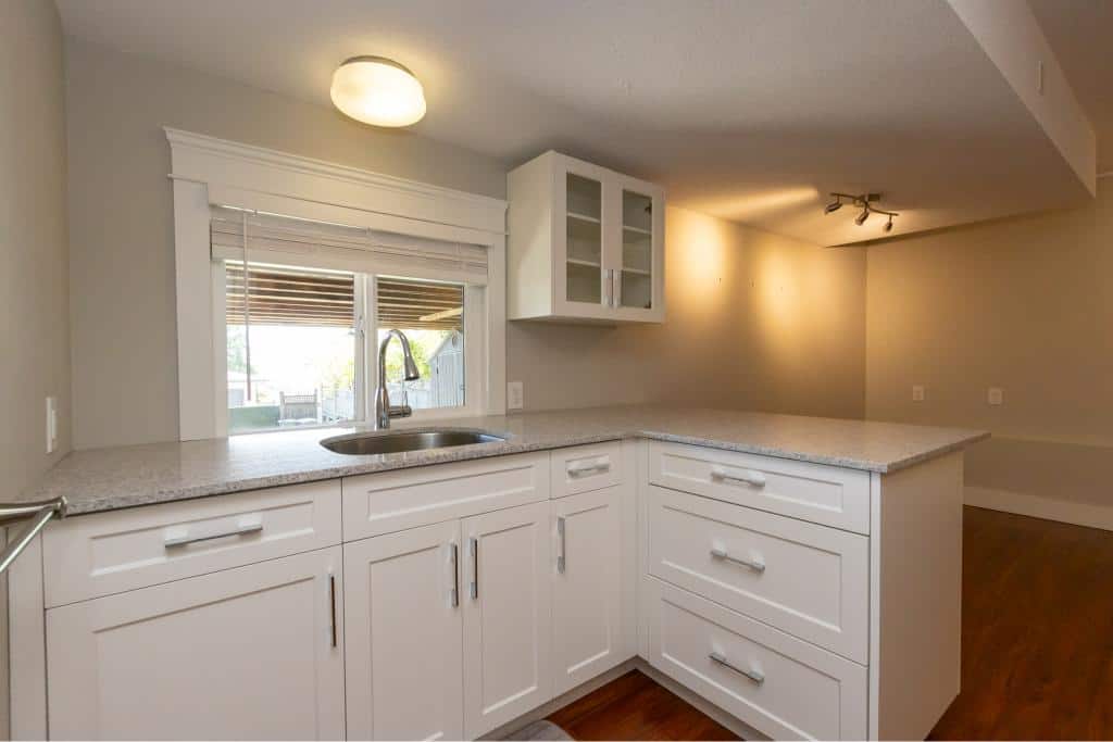 Modern kitchen with white cabinets and granite countertops, featuring a large window for natural light and stainless steel fixtures, ideal for homebuyers exploring Vancouver Island real estate.